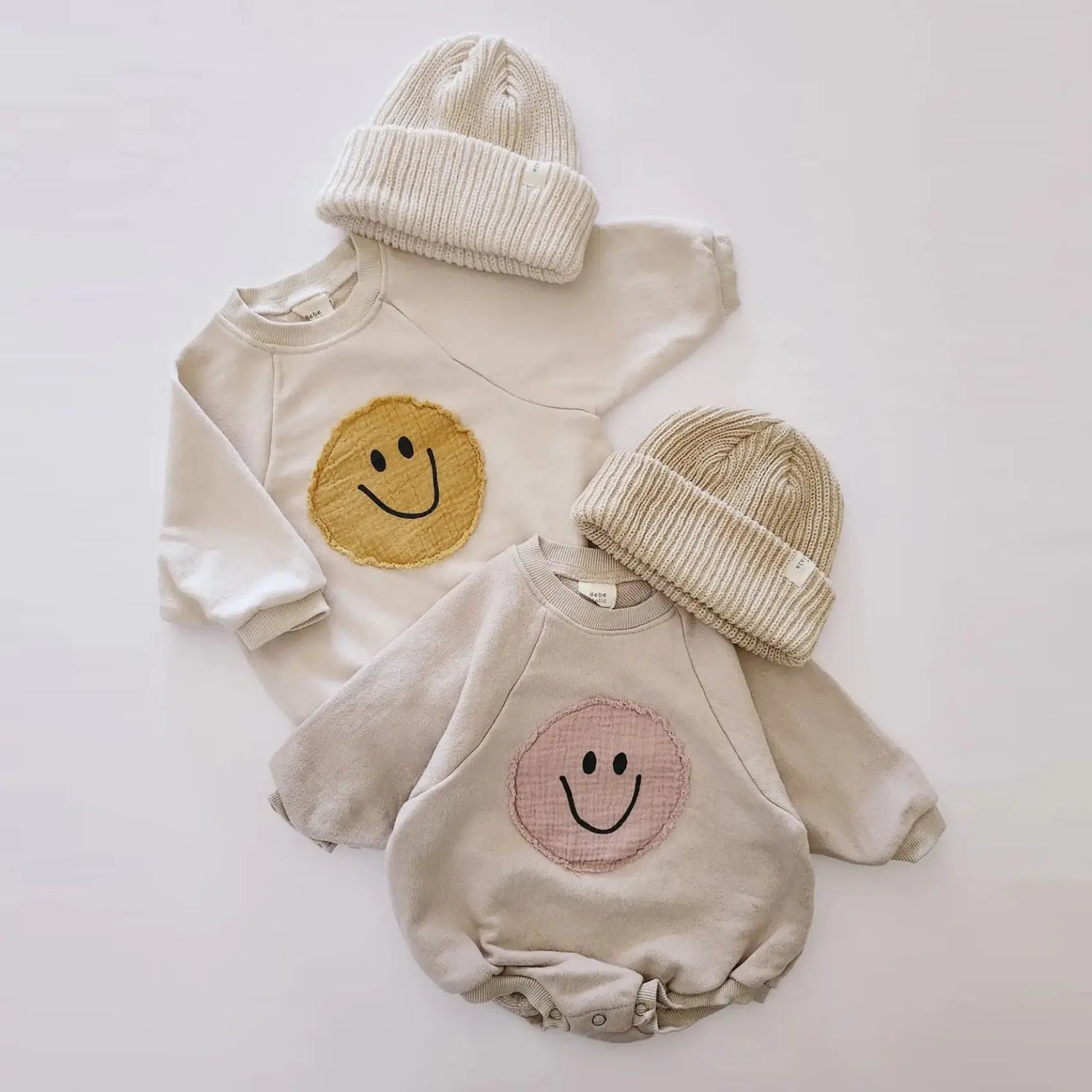 Infant Baby & Toddlers cream colored bubble romper with yellow and pink smiley faces from MilkBabyCo laid flat on a blank surface. 