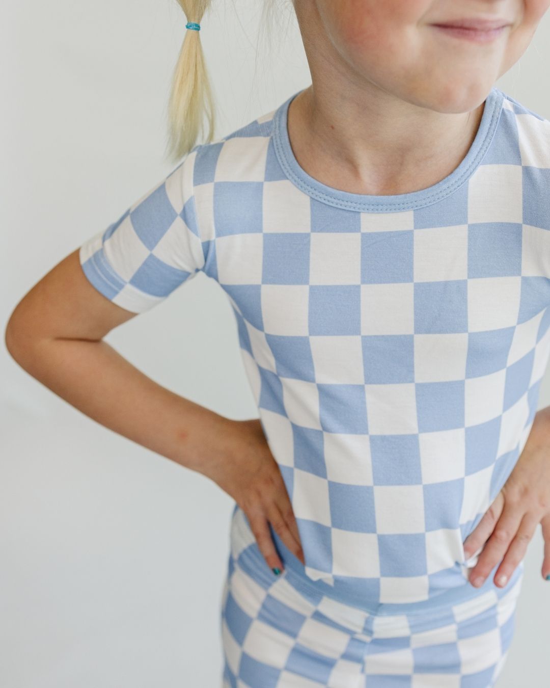 Close up image of a young girl with her hands on her hips. She is wearing the Lucky Panda Kids viscose bamboo two-piece short pajama set in a white and light blue checkered pattern.