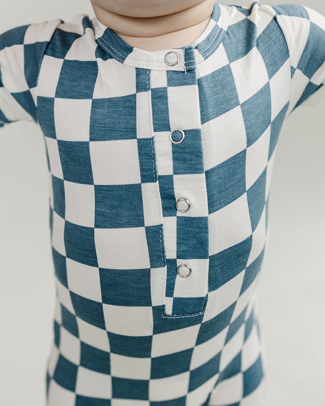 Close up upper half shot of a baby wearing the blue and white checkered short sleeve bamboo jumsuit from Lucky Panda Kids. Sold by MilkbabyCo