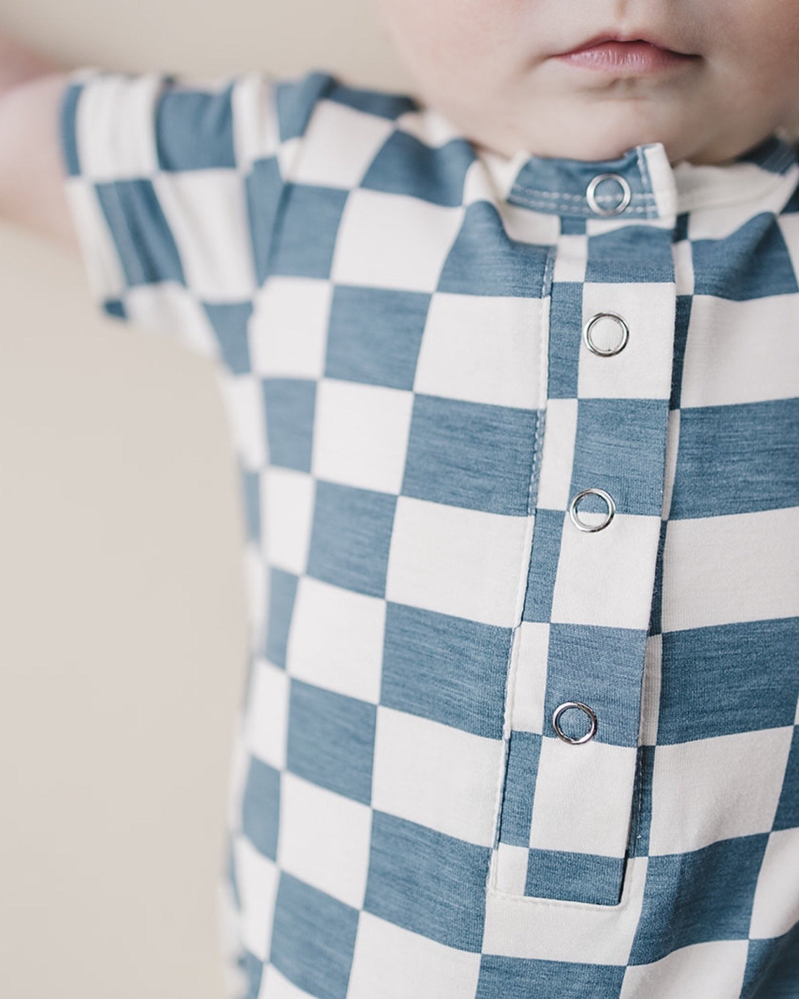 Close up shot of baby wearing blue and white checkered short sleeve bamboo jumsuit from Lucky Panda Kids. Sold by MilkbabyCo