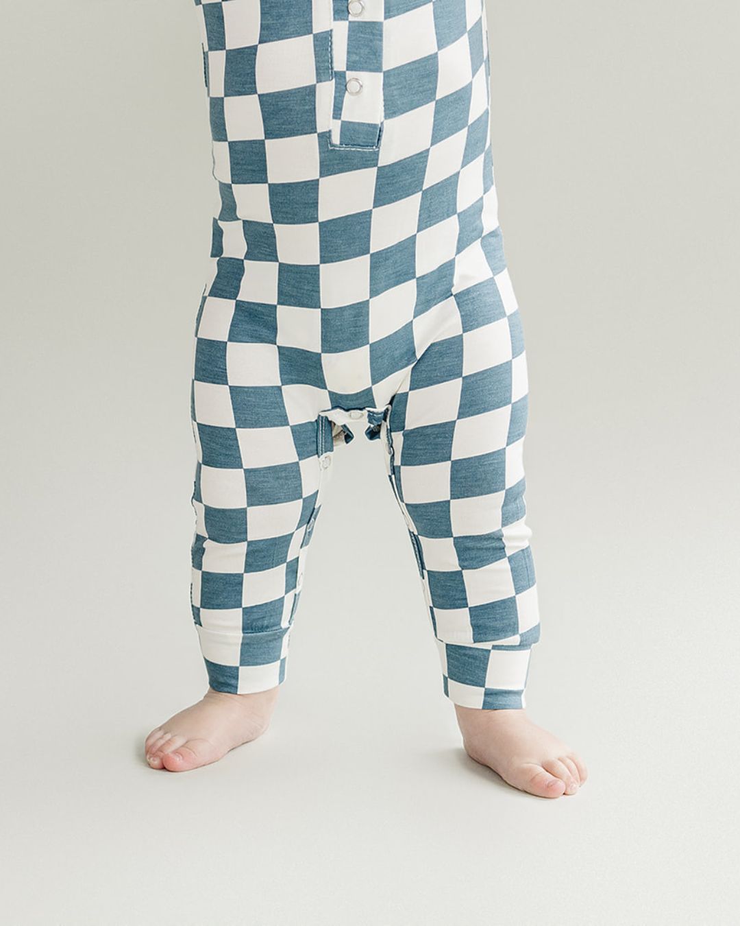 Close up lower half shot of baby wearing a blue and white checkered short sleeve bamboo jumsuit from Lucky Panda Kids. Sold by MilkbabyCo