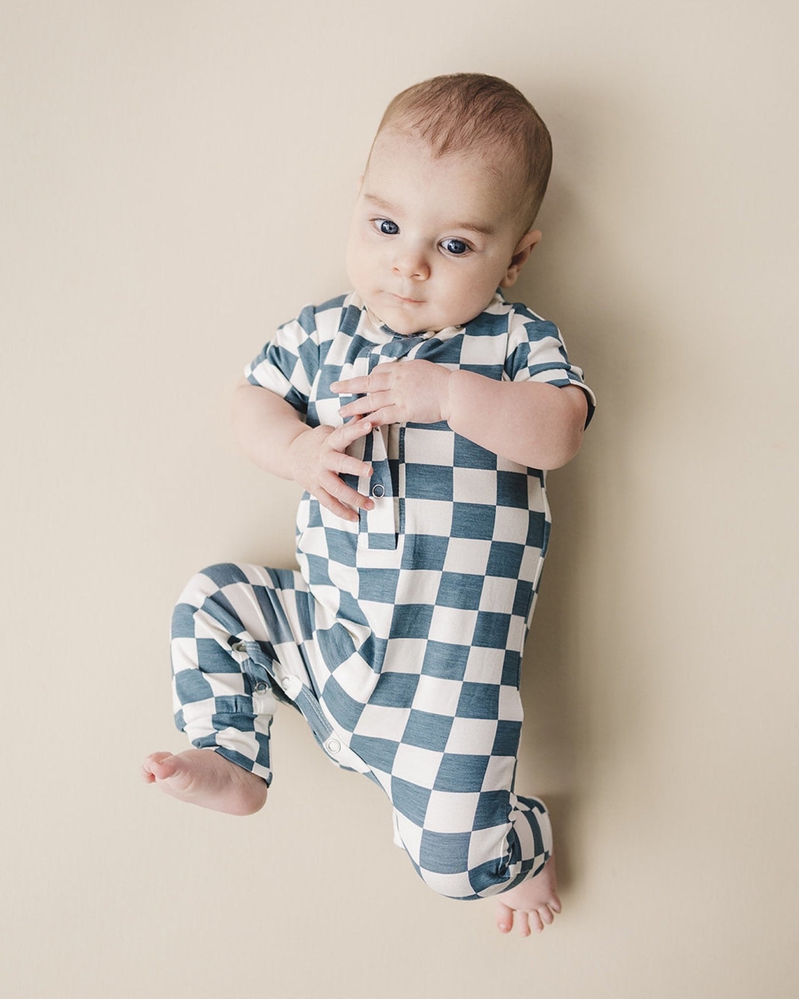 Baby laying down wearing blue and white checkered short sleeve bamboo jumsuit from Lucky Panda Kids. Sold by MilkbabyCo