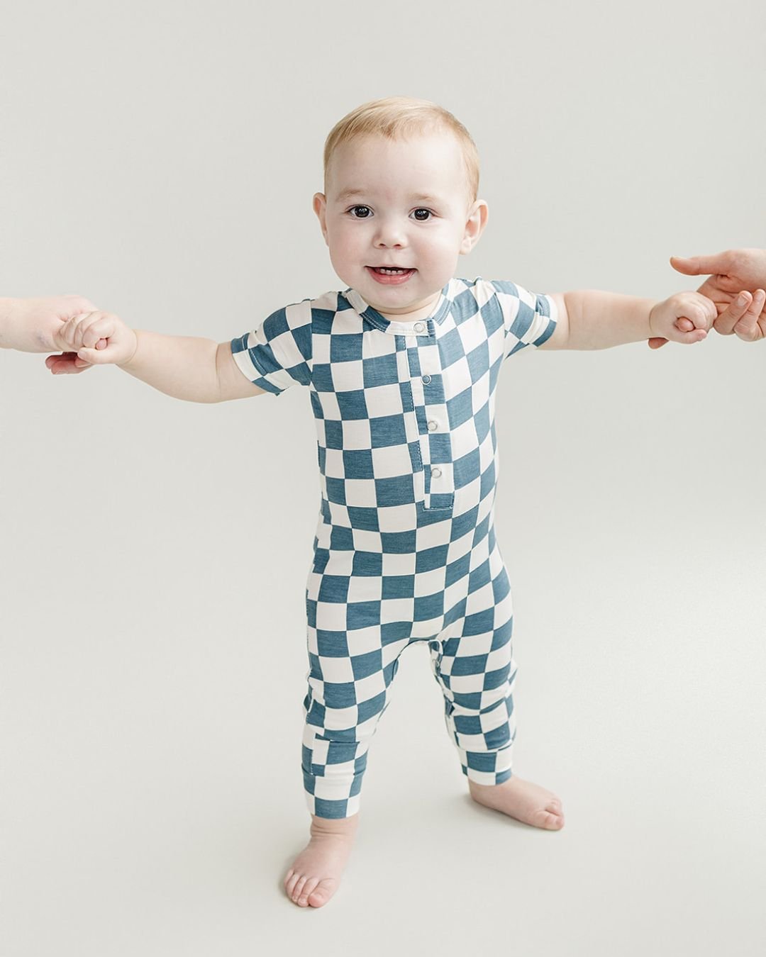 Baby standing up wearing blue and white checkered short sleeve bamboo jumsuit from Lucky Panda Kids. Sold by MilkbabyCo