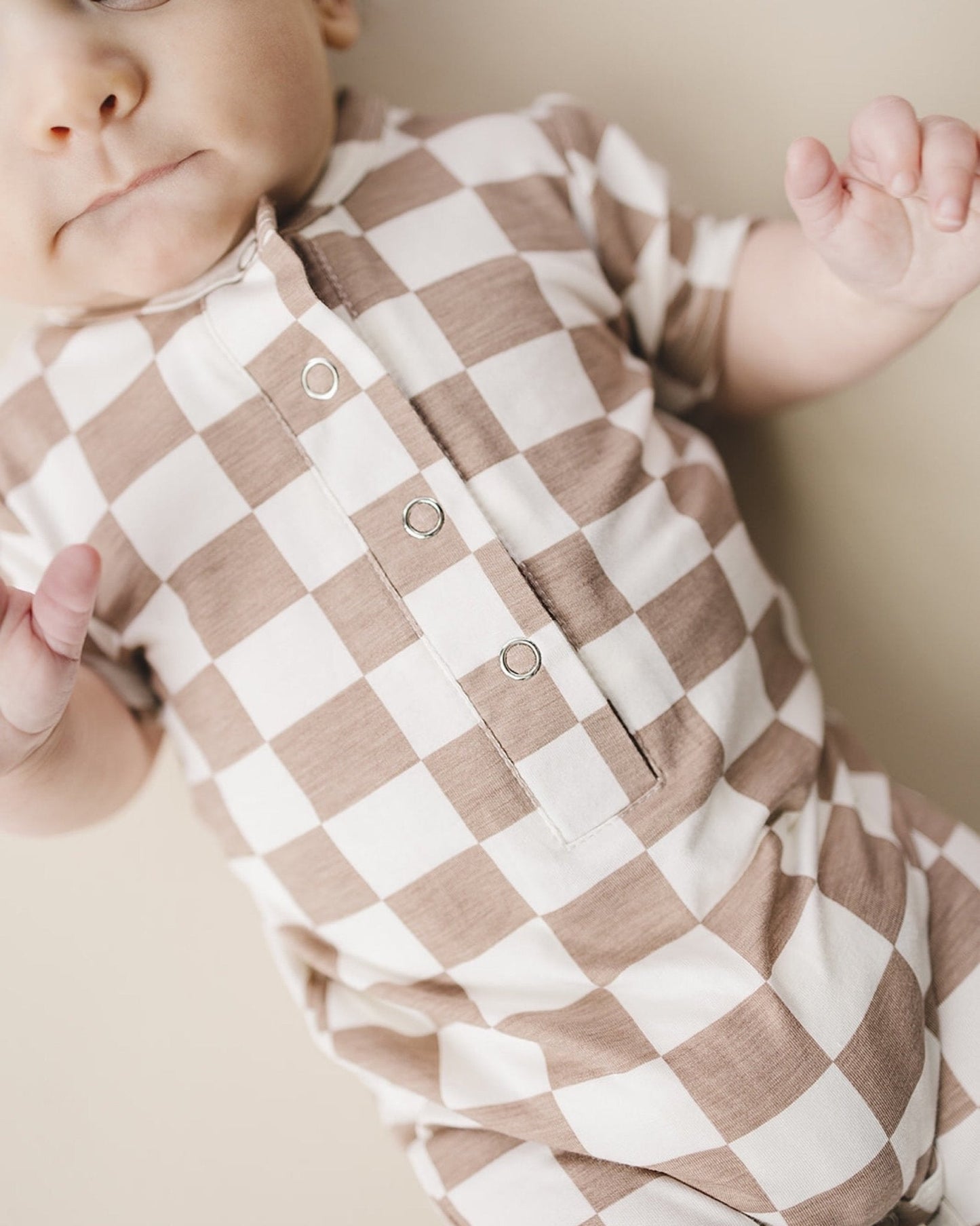 Close up of an infant baby laying down wearing a tan and white checkered short sleeve jumpsuit from Lucky Panda Kids made from soft viscose bamboo.