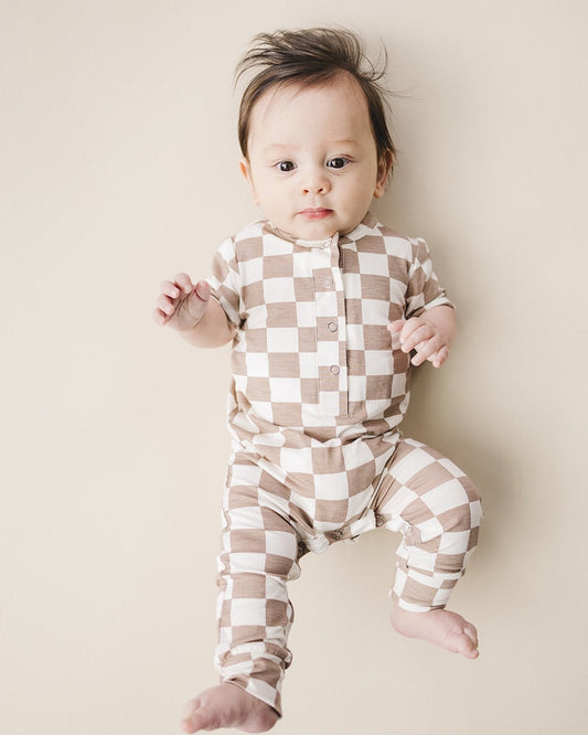 An infant baby laying down wearing a tan and white checkered short sleeve jumpsuit from Lucky Panda Kids made from soft viscose bamboo.