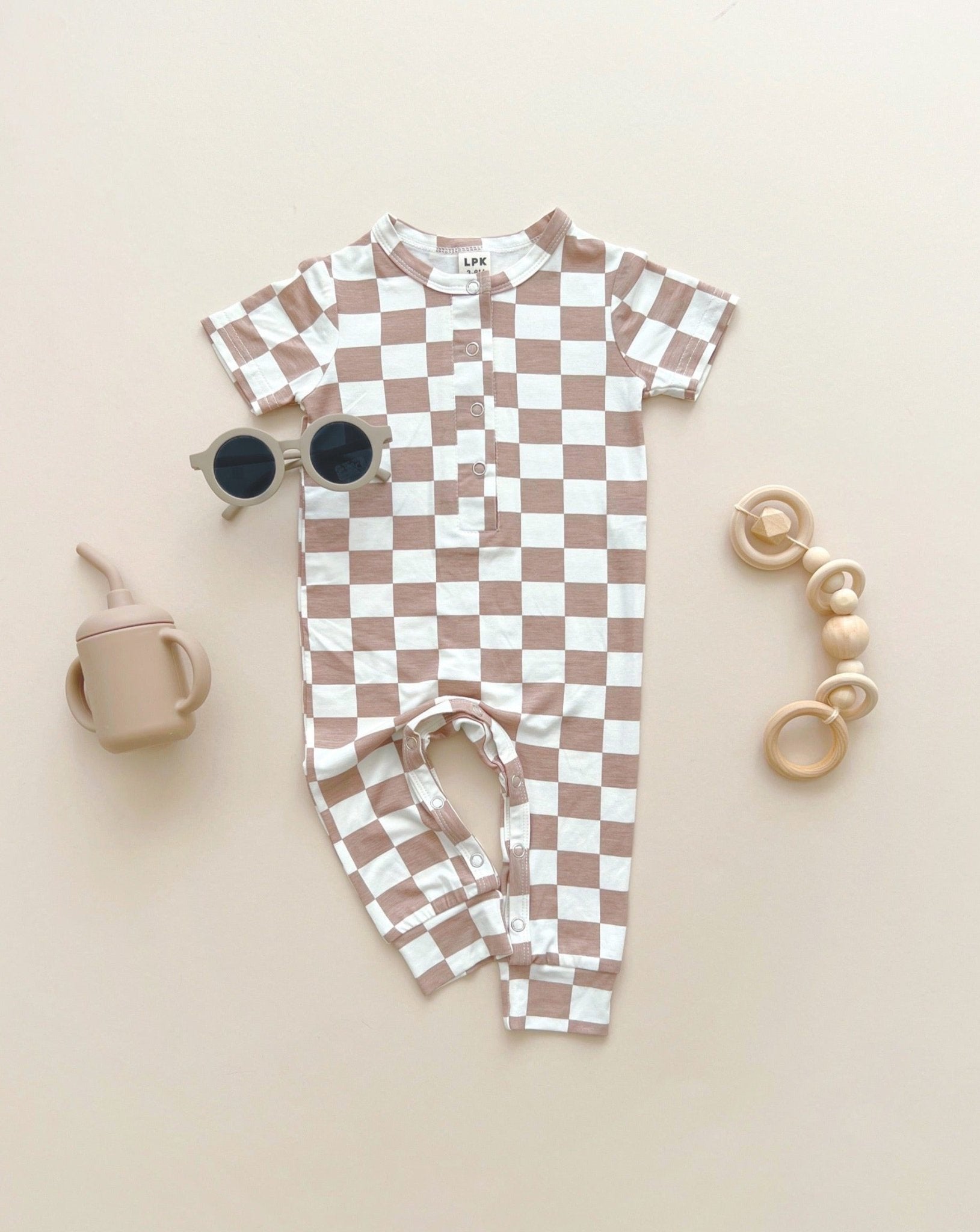 A tan and white checkered short sleeve jumpsuit from Lucky Panda Kids made from soft viscose bamboo laid out on a tan background.