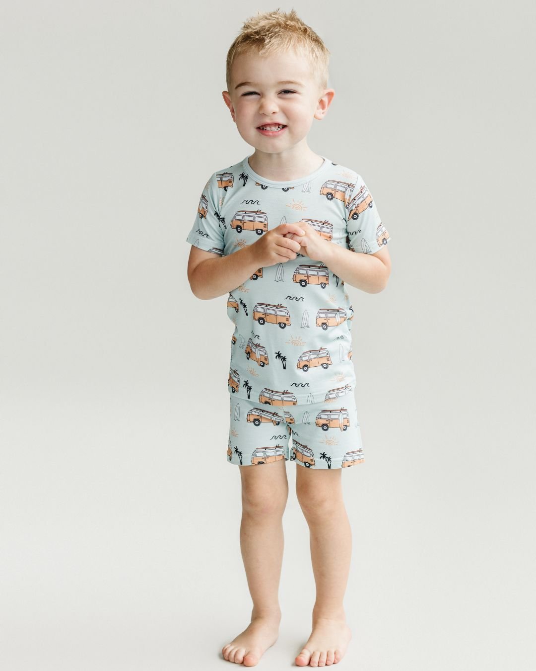 Little boy standing wearing the Lucky Panda Kids shorts set for babies and kids. He is wearing both a pair of shorts and a t-shirt that are blue with light orange surf vans and surf boards in the theme of california surf laid out on a blank background.