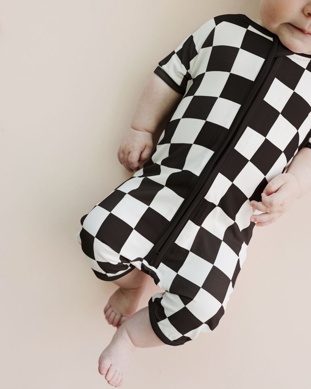 Infant baby boy laying down wearing a Lucky Panda Kids bamboo and cotton black and white checkered short sleeve shortie romper.