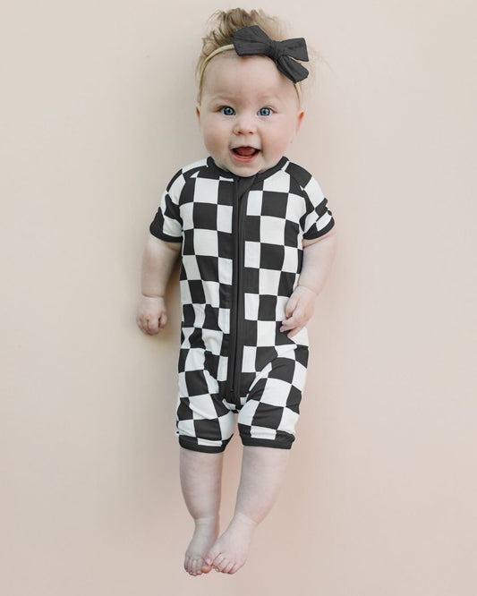 Infant baby girl laying down wearing a Lucky Panda Kids bamboo and cotton black and white checkered short sleeve shortie romper.