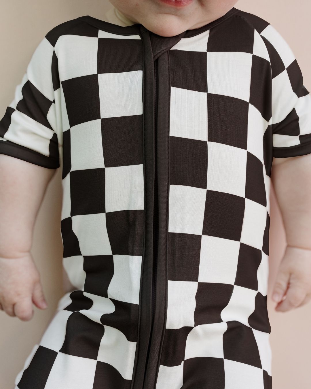 Close up shot of a baby wearing a Lucky Panda Kids bamboo and cotton black and white checkered short sleeve shortie romper.