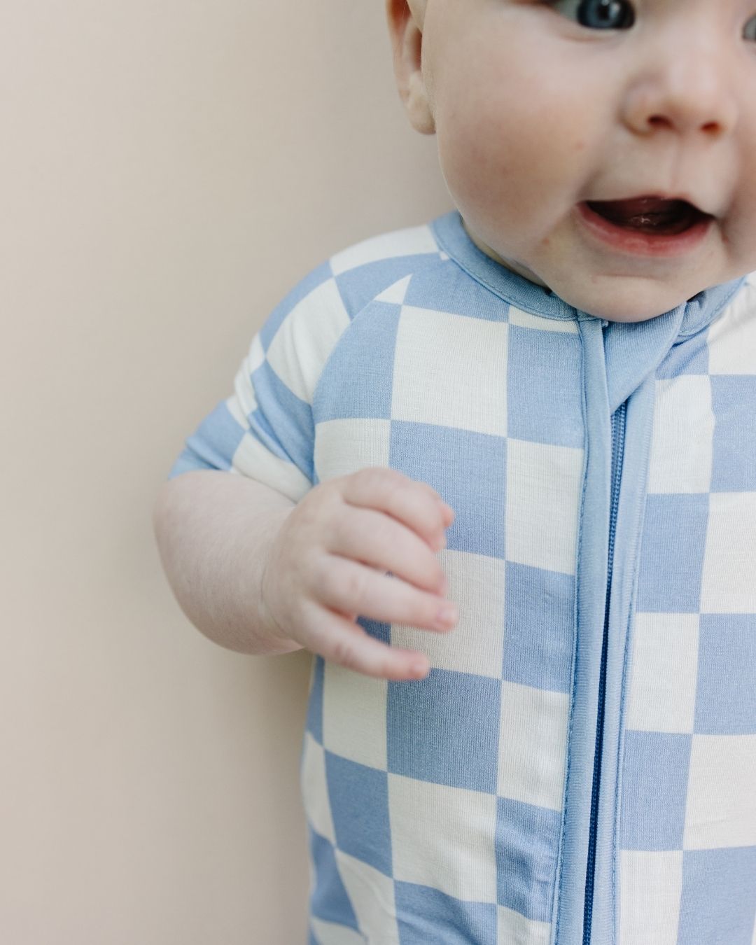 Close up shot of an Infant baby boy laying down wearing a Lucky Panda Kids bamboo and cotton blue and white checkered short sleeve shortie romper.