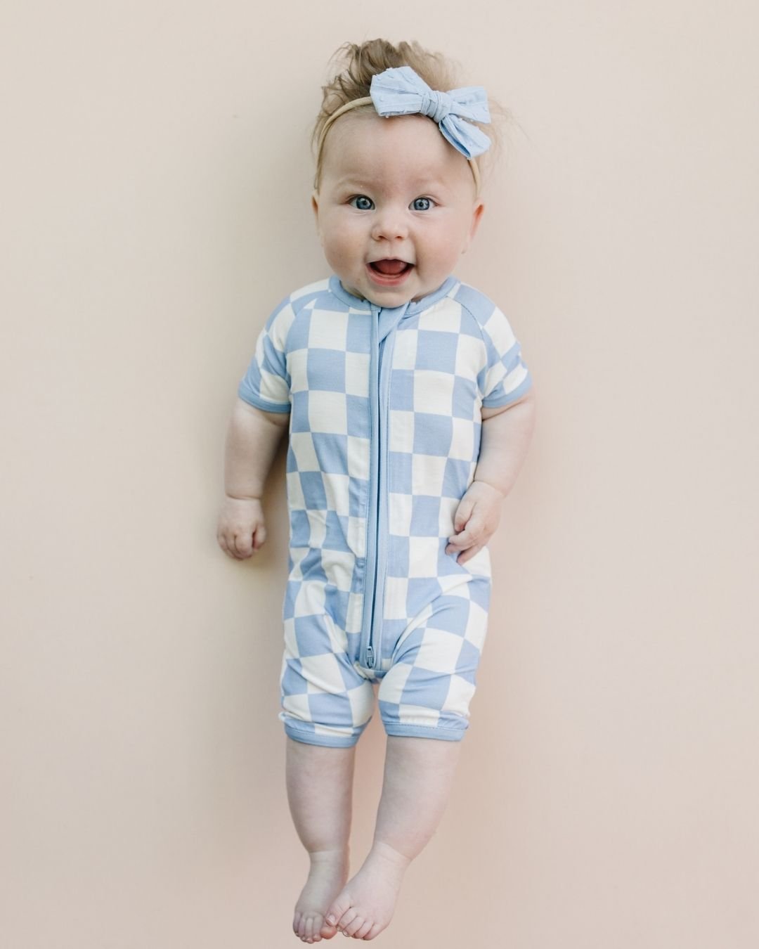 Infant baby girl laying down wearing a Lucky Panda Kids bamboo and cotton blue and white checkered short sleeve shortie romper.