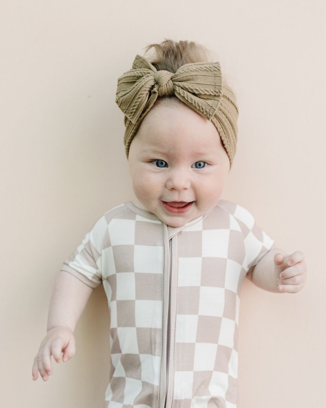 Upper half shot of an infant baby girl wearing a Lucky Panda Kids short sleeve bamboo shortie romper in white and tan checkered design. 