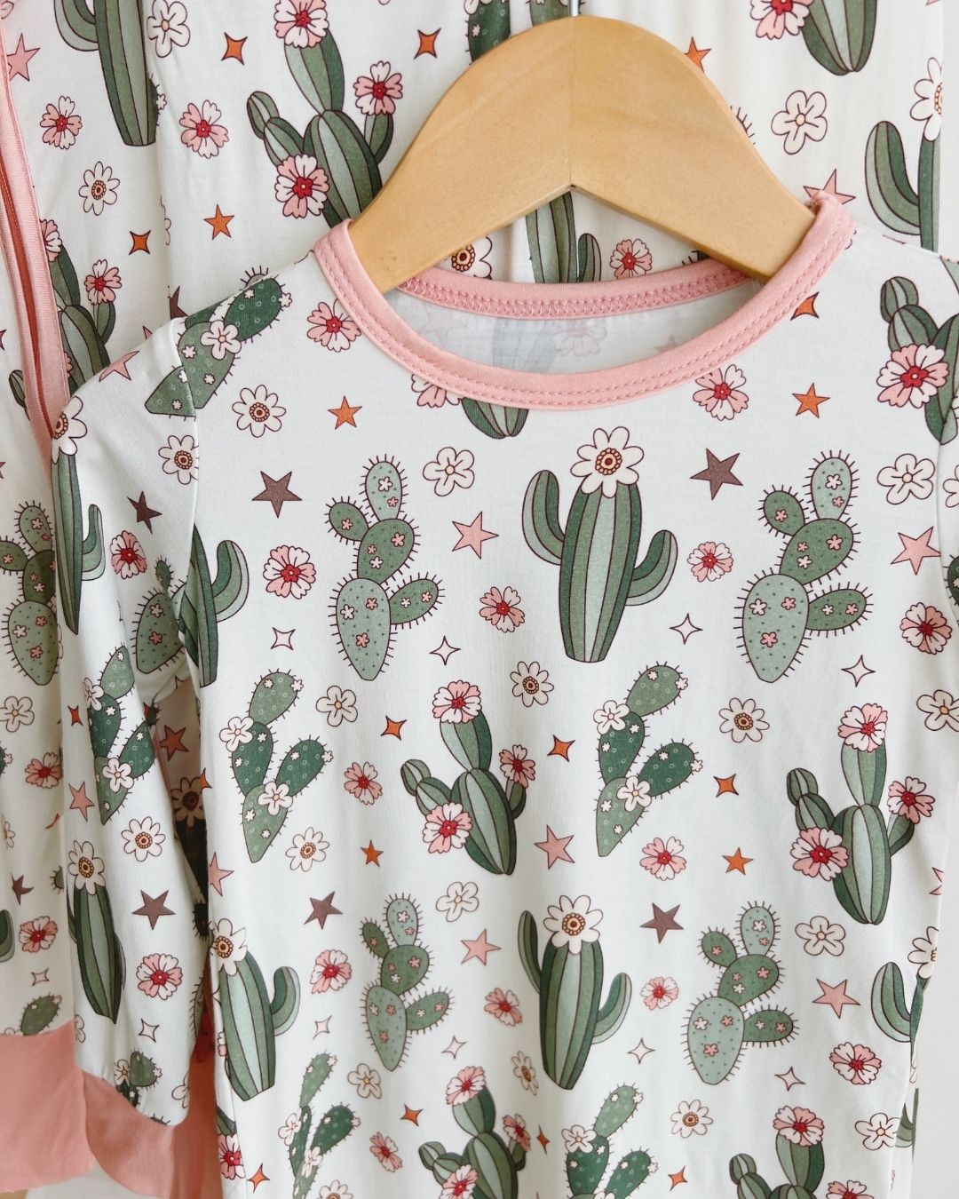 Close up image of the top of a two piece pajama set in cream color with light pink trim, green cactus designs with small pink flowers and stars. The pj's are part of the viscose bamboo collection from Lucky Panda Kids. 