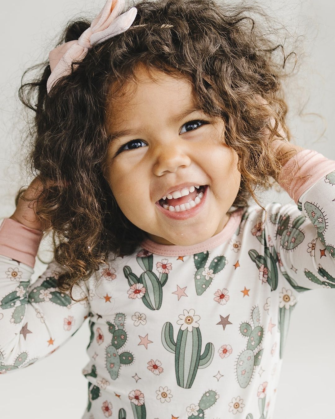 Close up headshot of a young girl standing up wearing a two piece pajama set in cream color with light pink trim, green cactus designs with small pink flowers and stars. The pj's are part of the viscose bamboo collection from Lucky Panda Kids. 