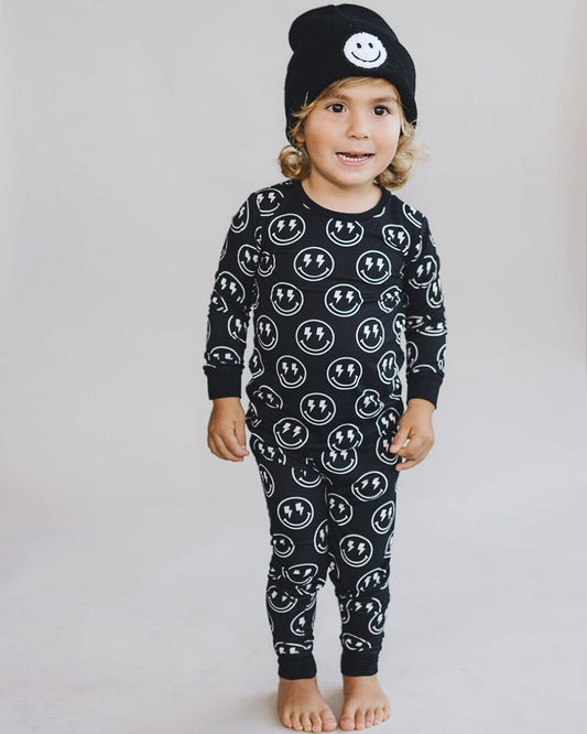 A young boy standing up wearing a two piece black viscose bamboo pajama set from Lucky Panda Kids with white smiley faces and lightning bolts for eyes on the pj's. 