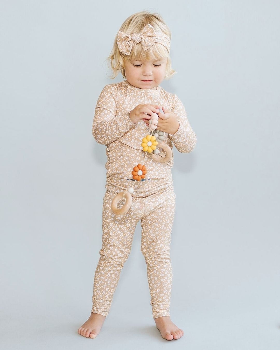 A young girl standing up wearing a two piece pajama set in tan, decorated with white small flowers all over. The pj's are from Lucky Panda Kids brand. 