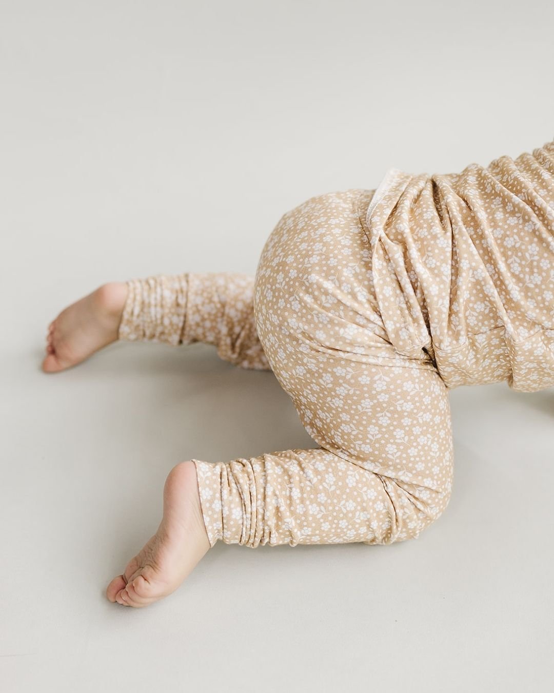 Lower half image of a baby girl crawling wearing a two piece pajama set in tan, decorated with white small flowers all over. The pj's are from Lucky Panda Kids brand. 