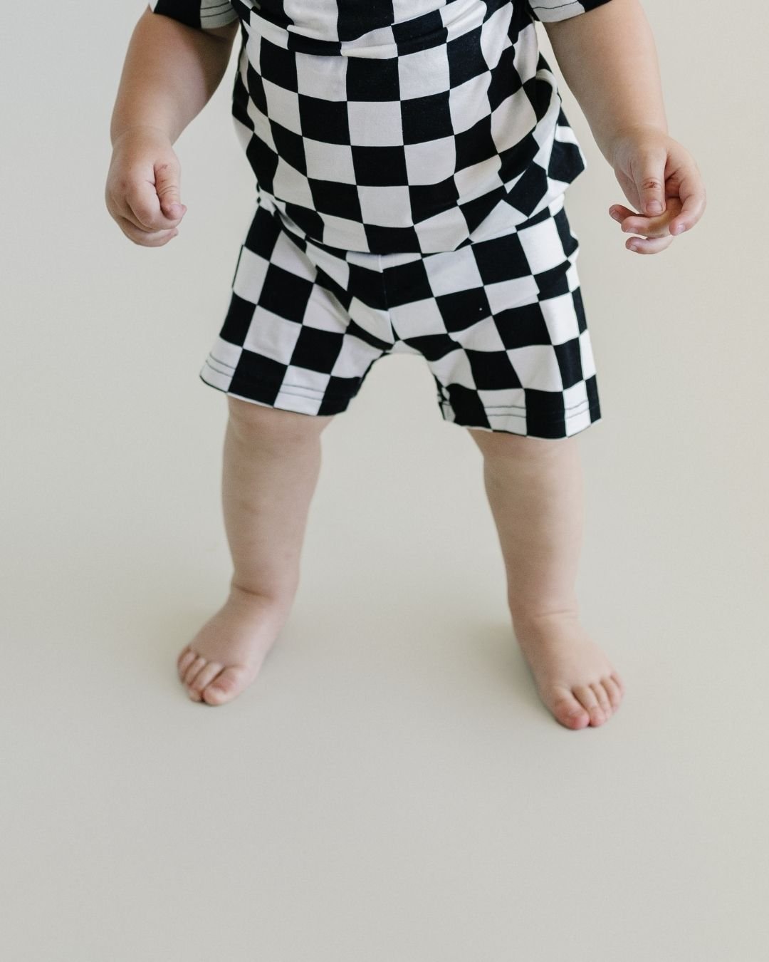 Headless close up shot of a baby standing. He is wearing a Lucky Panda Kids two-piece soft viscose bamboo pajama shorts set in a white and black checkered print.