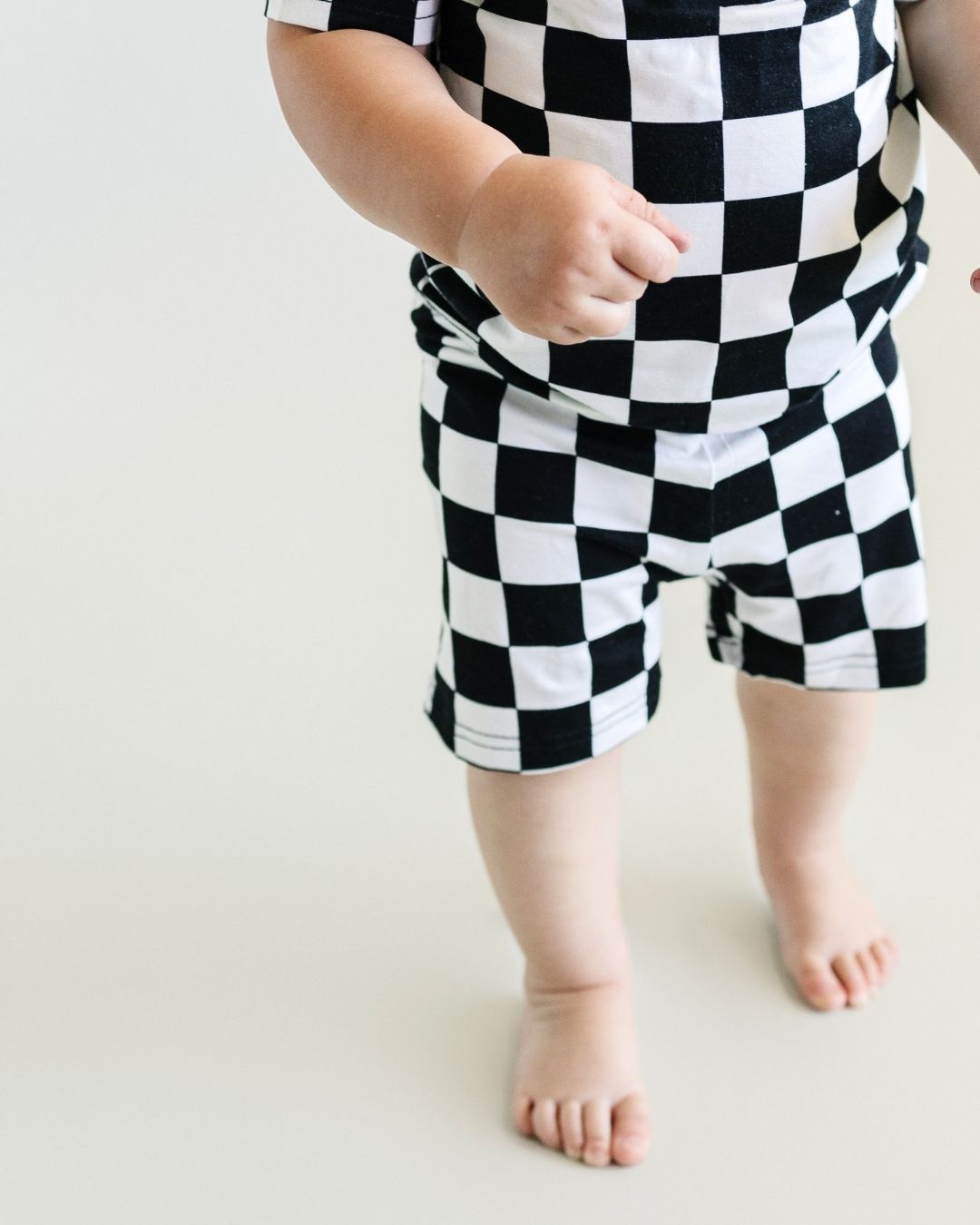 Close up shot of a baby boy wearing a Lucky Panda Kids two-piece soft viscose bamboo pajama shorts set in a white and black checkered print.