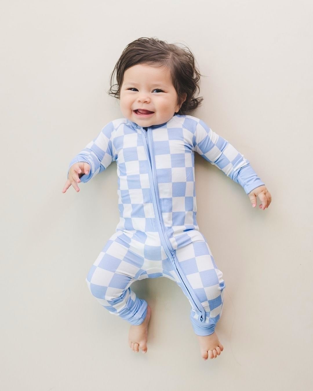 An infant baby laying on the floor on his back wearing the Lucky Panda Kids viscose bamboo two-piece pajama set in a white and light blue checkered pattern.