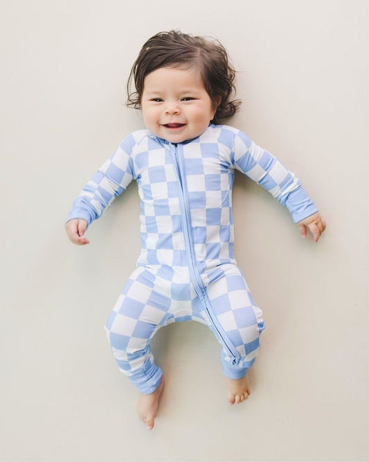 An infant baby laying on the floor on his back wearing the Lucky Panda Kids viscose bamboo two-piece pajama set in a white and light blue checkered pattern.