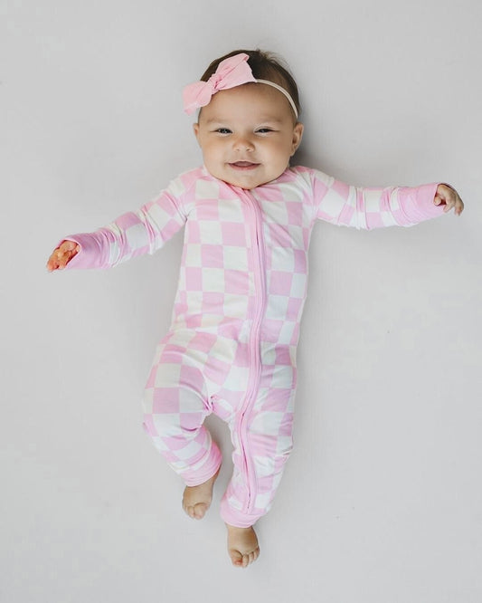 An infant girl laying down wearing a Lucky Panda Kids soft viscose bamboo zip up pajama in a white and light pink checkered pattern.