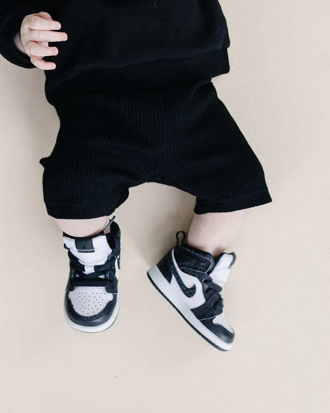 Close up body shot of a baby boy laying down wearing a black cotton Lucky Panda Kids "Biker Set" which includes ribbed cotton shorts and a sweatshirt with a fuzzy white smiley face emblem on the top right.