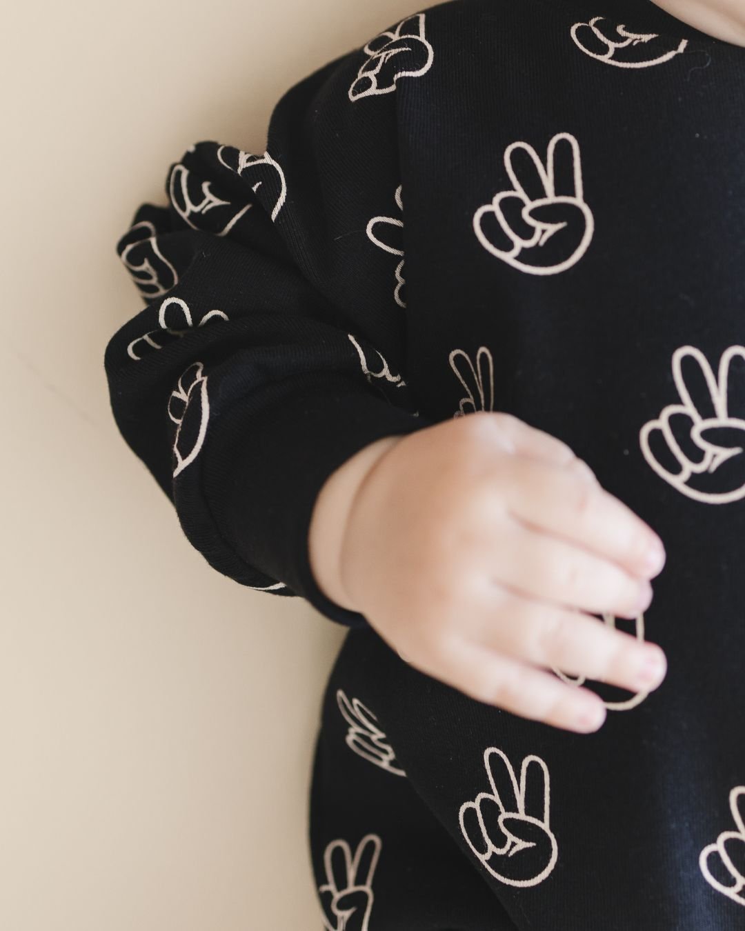 Headless close up detail image of an infant baby boy laying down wearing the long sleeve cotton black bubble romper from Lucky Panda Kids with white peace signs printed on it. 