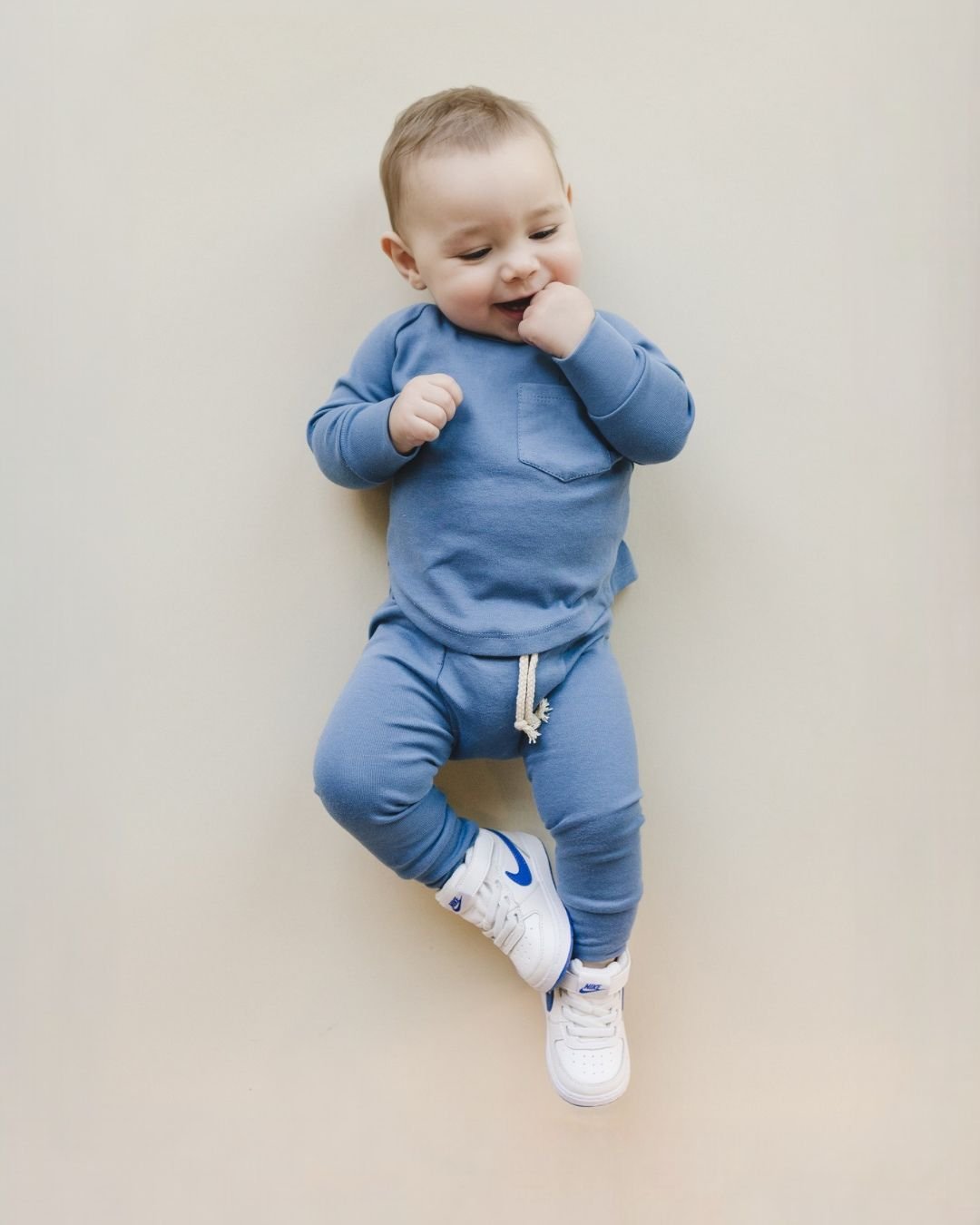 Baby boy laying down on his back with his hand in his mouth. He is wearing the cotton Ocean Blue Lounge Set from Lucky Panda Kids which includes a pair of pants and a long sleeve shirt that match. 